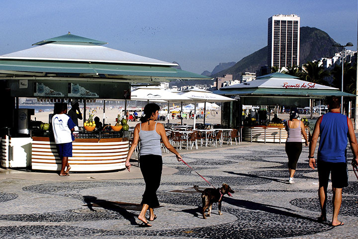 Fotografia de pessoas caminhando no calçadão da praia de Copacabana no Rio de Janeiro.