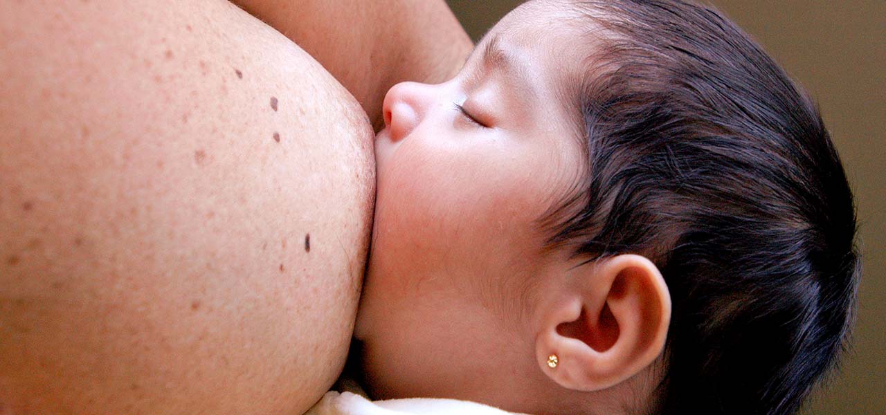 Fotografia de um bebê sendo amamentado no seio materno.