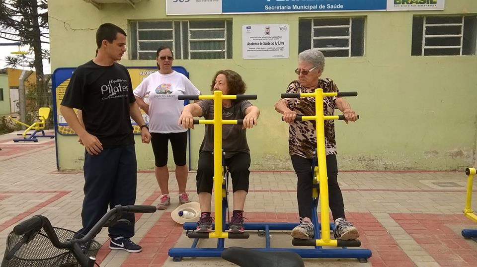 Fotografia de três mulheres praticando atividade física com a supervisão de um profissional de saúde.