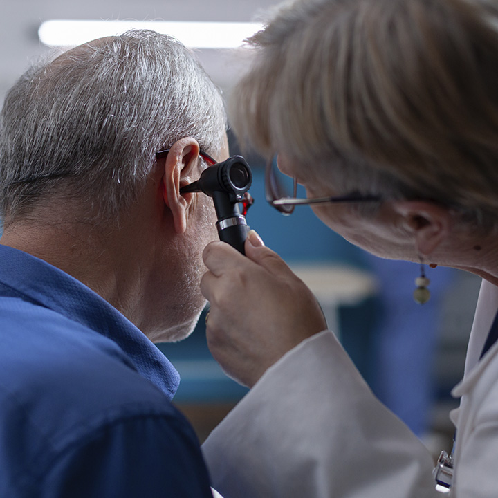 Fotografia em que uma profissional de saúde examina o ouvido de um homem utilizando um otoscópio.