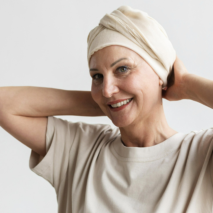 Fotografia de uma mulher branca sorrindo utilizando um turbante na cabeça, similar ao que mulheres em tratamento de quimioterapia costumam utilizar.