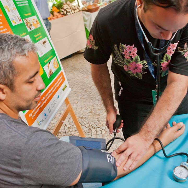 Fotografia em que um homem tem sua pressão arterial aferida por outro homem.