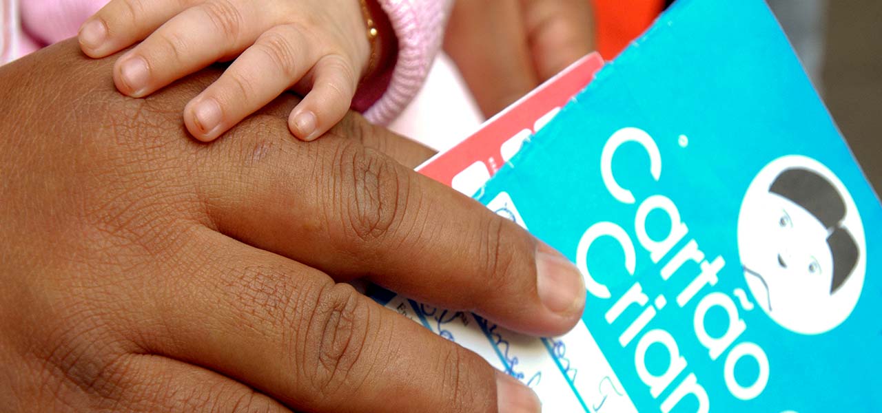 Fotografia do Cartão da Criança na mão de uma pessoa adulta, que segura também a mão de um bebê.