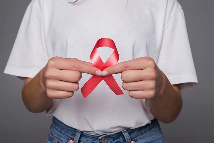 Fotografia de pessoa segurando uma fita vermelha da campanha de prevenção ao HIV.