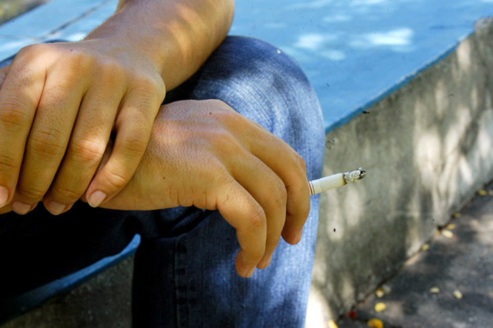 Fotografia de mãos de uma pessoa segurando um cigarro aceso.