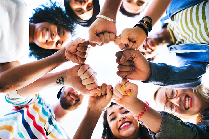 Fotografia de um grupo de jovens sorridentes unindo seus punhos um ao lado do outro no centro da imagem.
