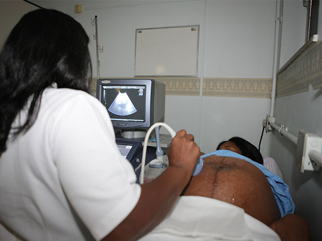 Fotografia de uma profissional de saúde realizando o exame de ultrassom abdominal em uma gestante negra.