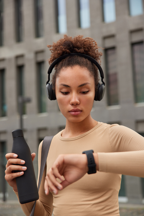 Fonte: Freepik.com Fotografia de uma mulher negra com o cabelo preso usando fones, segurando uma garrafa d’água e olhando para seu wearables.