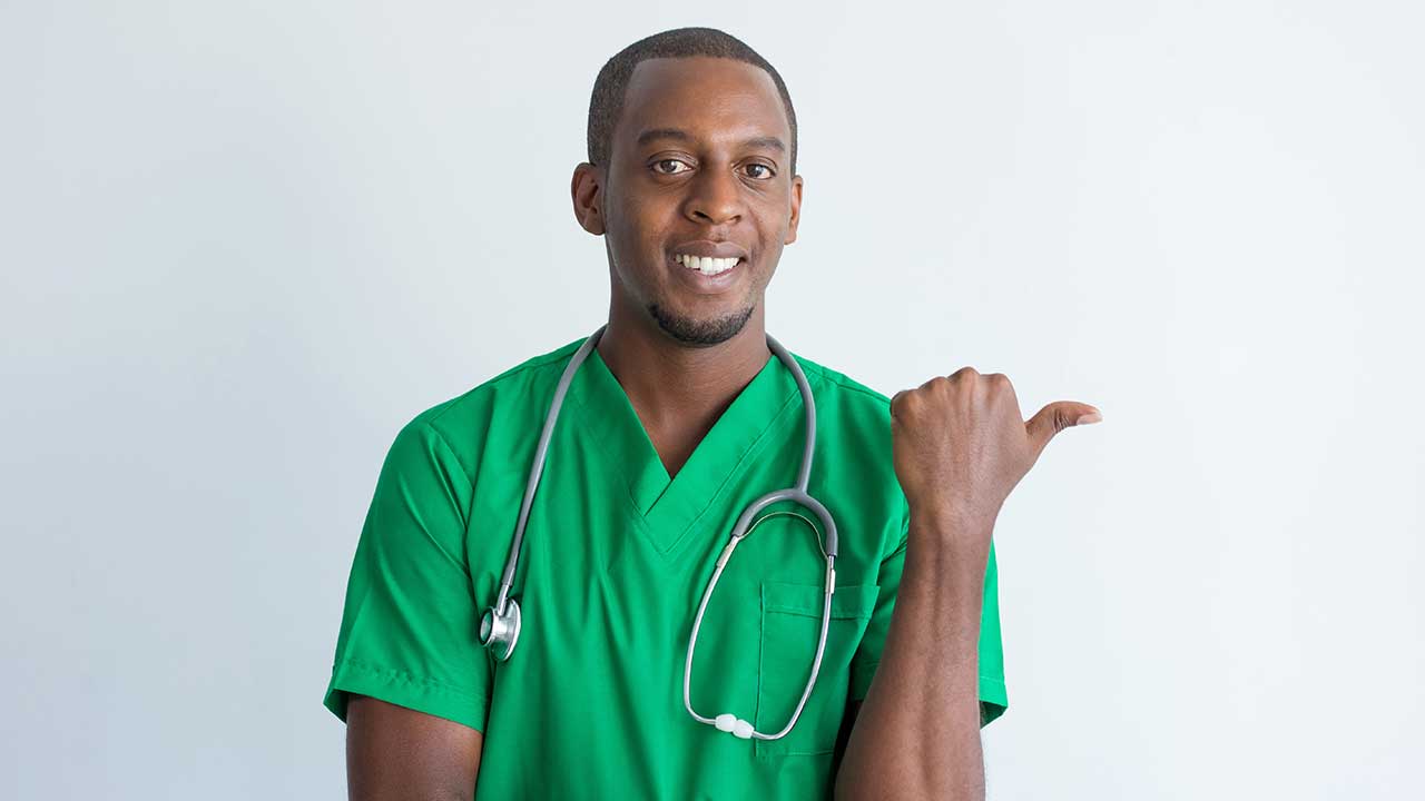 Fotografia de um homem negro usando uniforme verde da área da saúde, com um estetoscópio ao redor do pescoço, ele sorri.